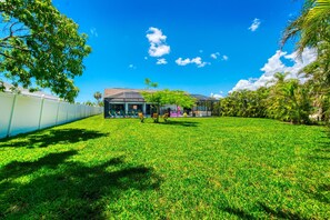 A grassy area with a building in the background, a fence, and trees. - "Hello Sunshine is 20 minutes from Fort Myers Beach. (Cape Coral)
