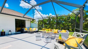 Eine Terrasse im Freien mit weißen Korbmöbeln, gelben Kissen und einer Glaskonstruktion.