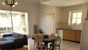 A living room with a sofa, a dining table with chairs, a chandelier, and a kitchen area with cabinets and a sink. - SPACIOUS GITE WITH GARAGE (Talairan)