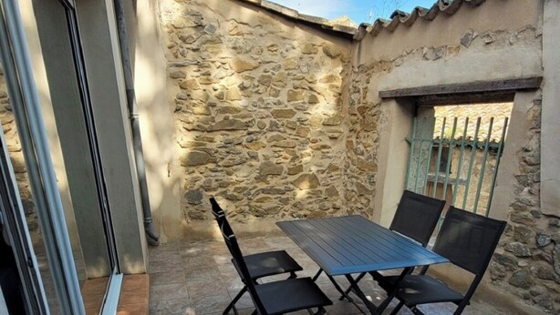 A patio with a table and chairs, stone walls, and a window with a metal gate. - SPACIOUS GITE WITH GARAGE (Talairan)