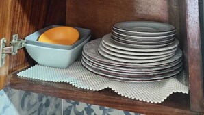 Un meuble en bois avec une étagère contenant un pot noir, un bol noir et une pile d’assiettes.