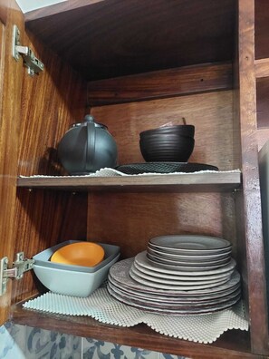 A wooden cabinet with a shelf containing a black pot, a black bowl, and a stack of plates.