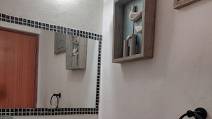 Une salle de bain avec un lavabo blanc, un plan de toilette noir et un miroir au-dessus. On y trouve un porte-serviettes sur lequel est accrochée une serviette.