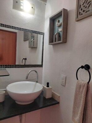 A bathroom with a white sink, black countertop, and a mirror above it. There is a towel rack with a towel hanging on it.