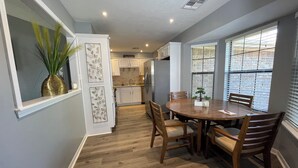 A dining area with a wooden table and chairs, a vase with green plants, and a kitchen in the background. - Relaxation, Comfort & Style (Lawton)