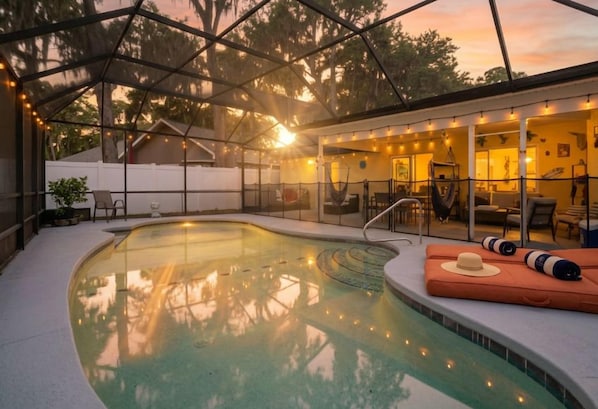 A pool area with a covered seating area, lounge chairs, and a hammock.