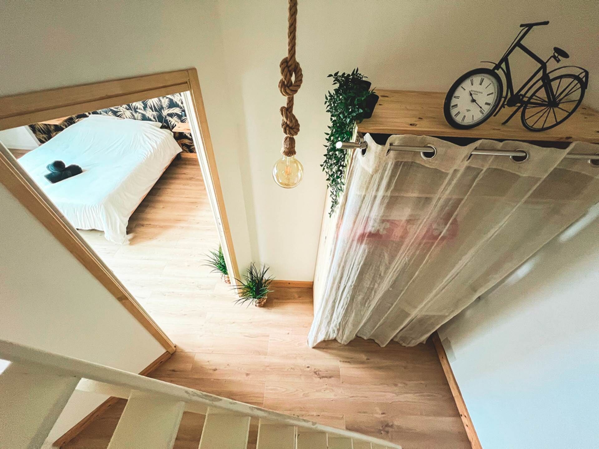 Een slaapkamer met een bed, een hanglamp, een fiets en een gordijn.
