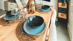 Un comedor con una mesa de madera preparada para cuatro, una escalera y un televisor montado en la pared.