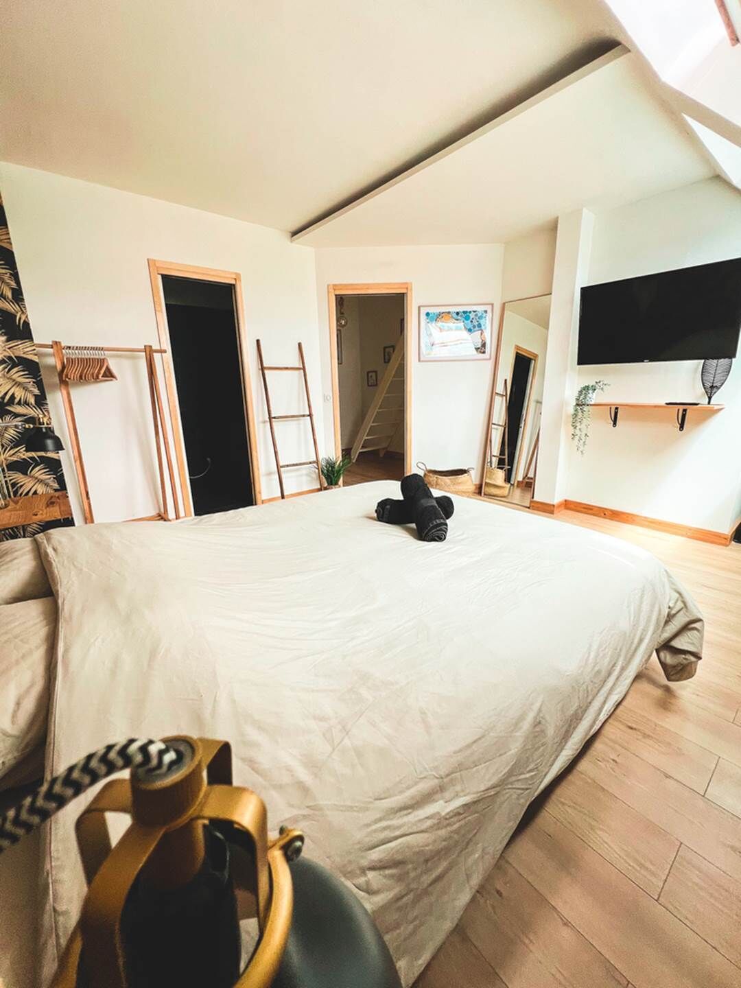 Quarto com uma cama grande, televisão fixada na parede e escada que leva a outro cômodo.