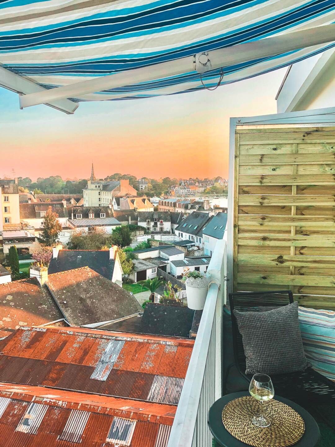 Ein Balkon mit Blick auf eine Stadt, eine Holzvertäfelung und ein Weinglas auf einer gewebten Matte.