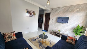 A modern living room with a dark blue sofa set, a coffee table, and a flat-screen TV mounted on the wall. - Abba nest, Enjoy a home away from home (Kampala)