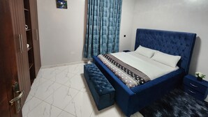 A bedroom with a blue bed, a wooden wardrobe, a small bedside table, and a nightstand. - Abba nest, Enjoy a home away from home (Kampala)