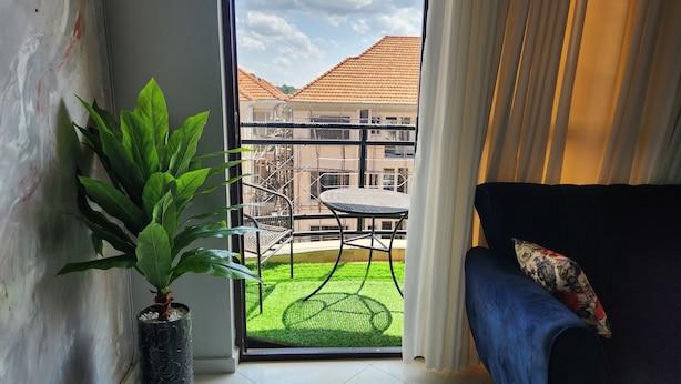 A balcony with a view of buildings, a potted plant, a chair, and a sofa. - Abba nest, Enjoy a home away from home (Kampala)