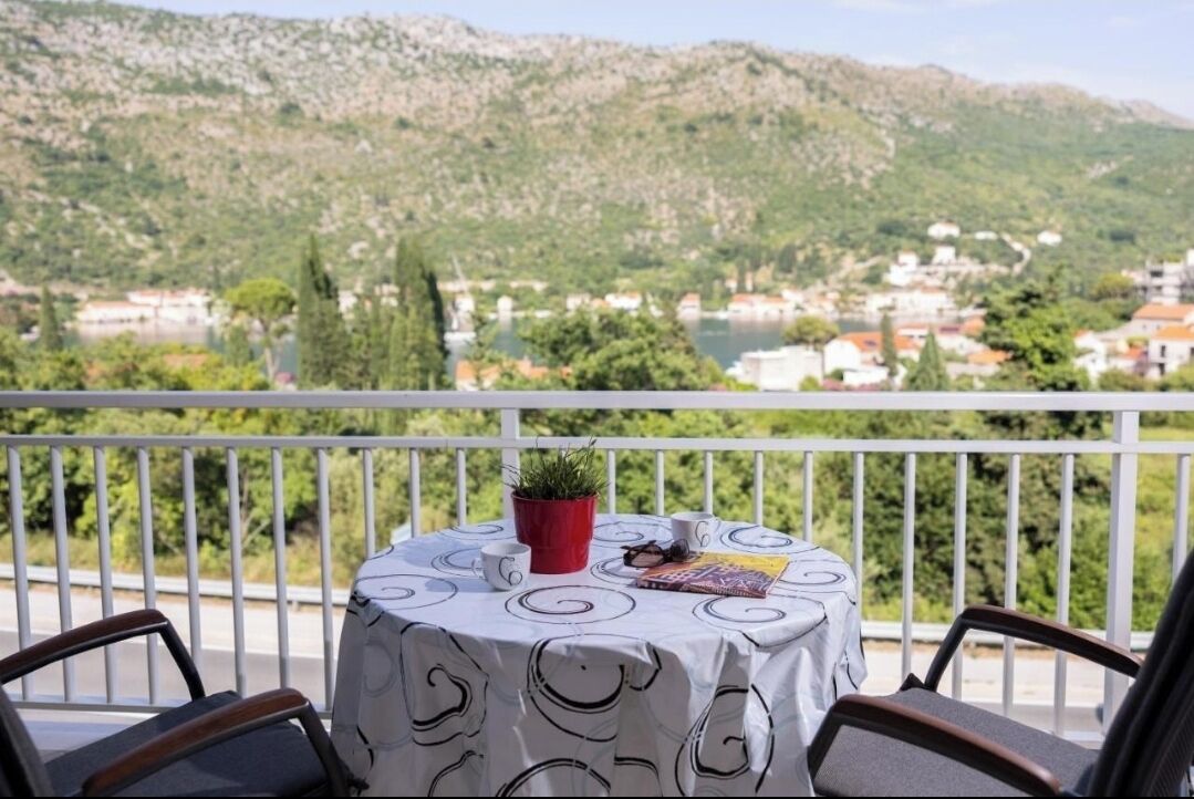 Un balcon avec une table dressée pour deux personnes, une plante en pot et un livre.
