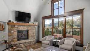 A cozy living room with a stone fireplace, comfortable seating, and a large window offering a mountain view.