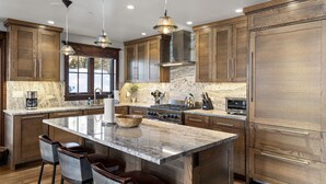 A modern kitchen with wooden cabinets, a large island with bar stools, stainless steel appliances, and pendant lighting.