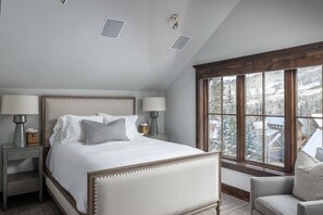 A bedroom with a large bed, two bedside tables with lamps, a window with a view of a snowy landscape, and a chair. - The Veranda at Trails Edge - penthouse views! (Mountain Village)