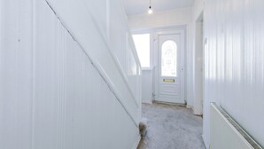 Un couloir étroit aux murs blancs, avec une porte blanche au fond.