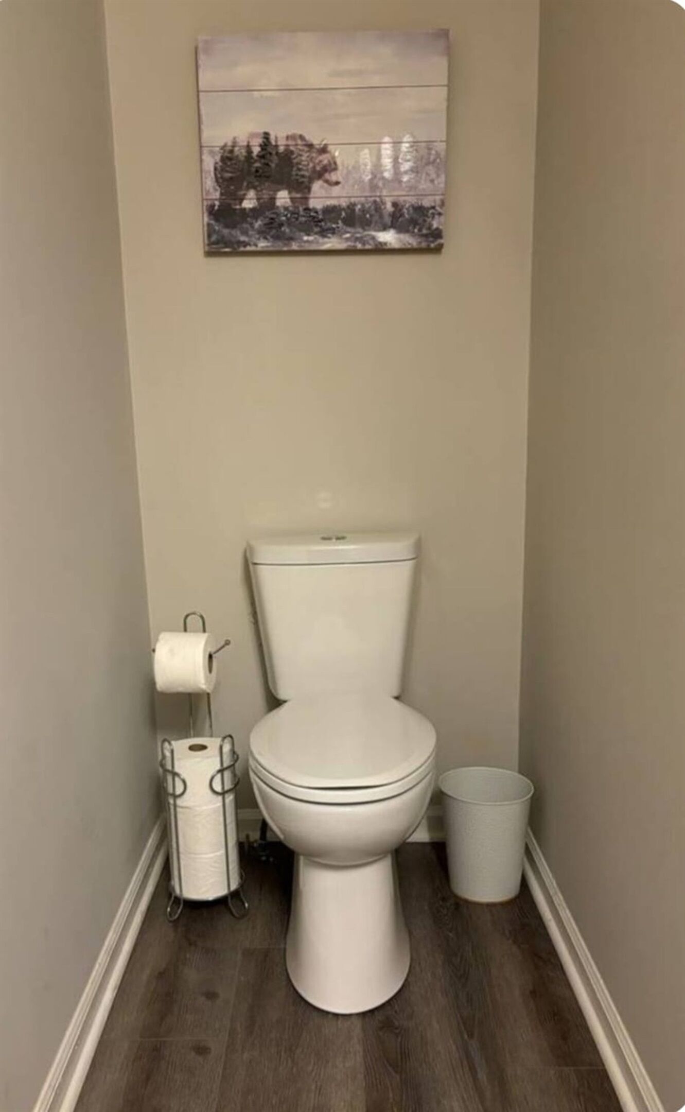 A small, narrow bathroom with a toilet, a toilet paper holder, and a trash can.
