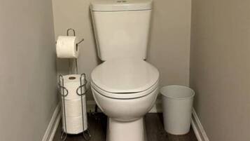A small, narrow bathroom with a toilet, a toilet paper holder, and a trash can.