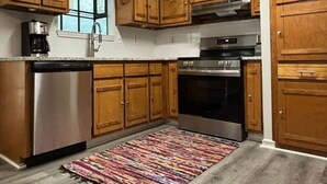 A kitchen with wooden cabinets, a stainless steel dishwasher, an oven, and a colorful rug.