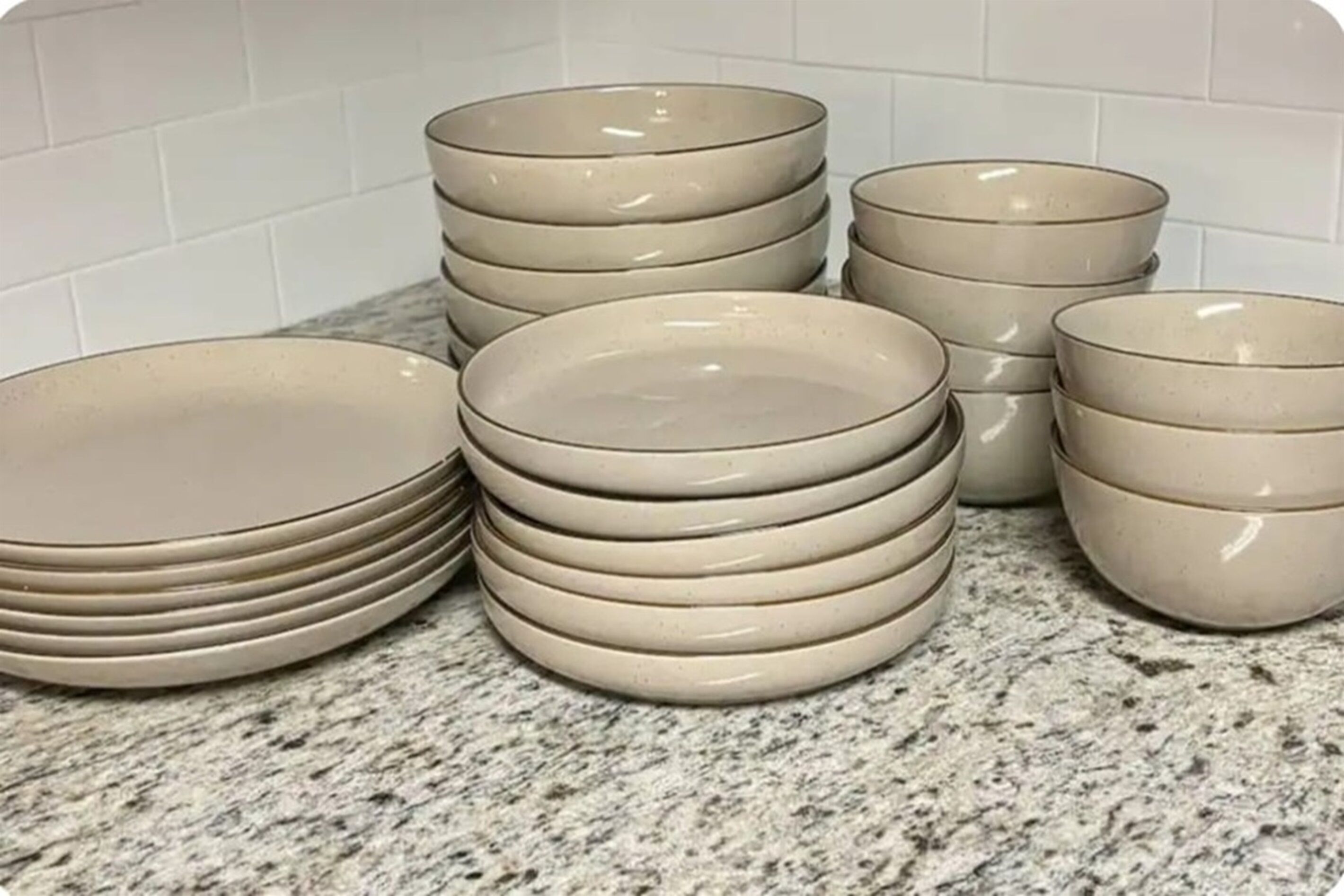 Een stapel beige borden en kommen op een granieten aanrecht.