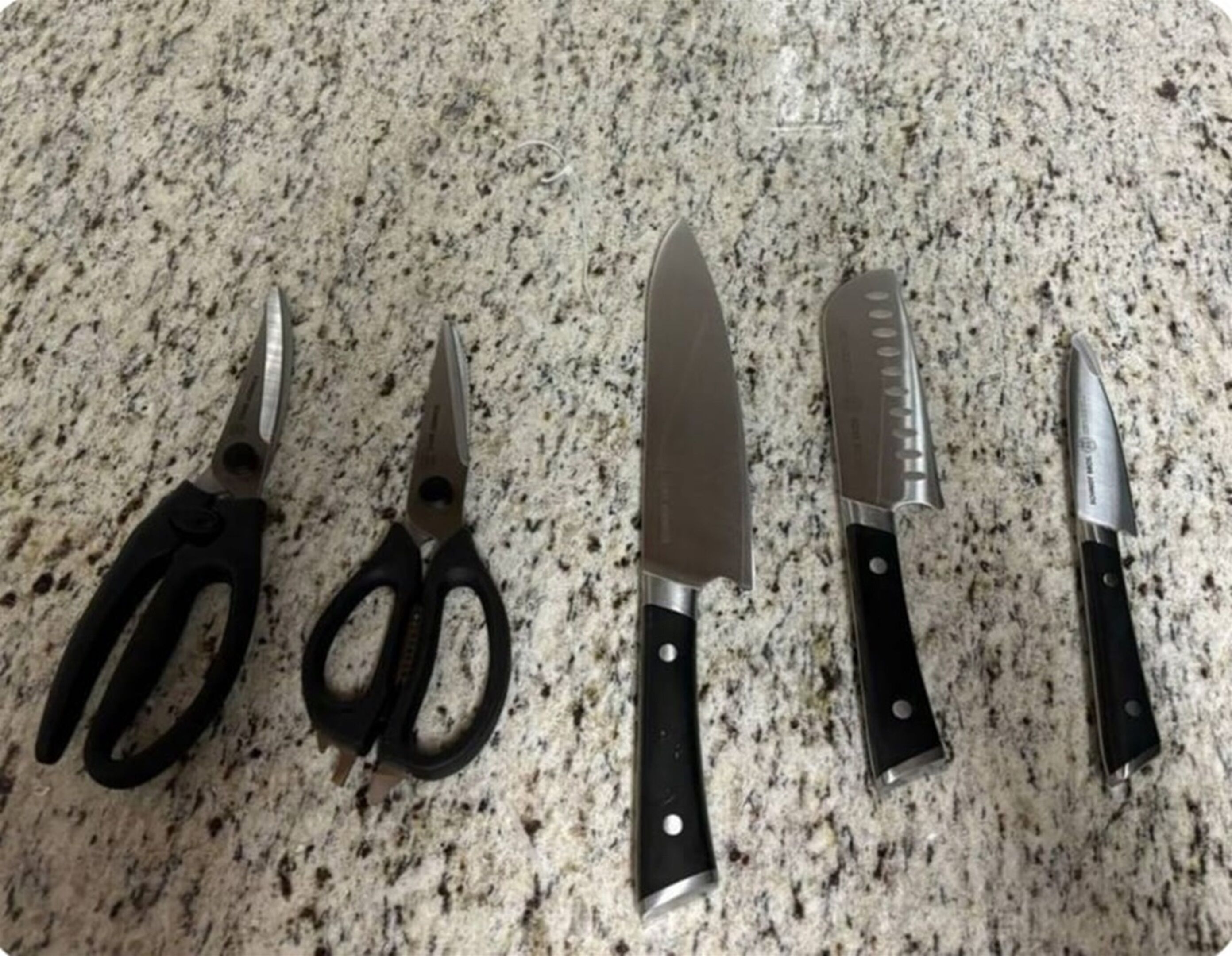 A set of kitchen knives and scissors on a granite countertop.