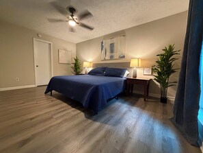 Un dormitorio con cama, dos mesitas de noche, un ventilador de techo y dos plantas en macetas.