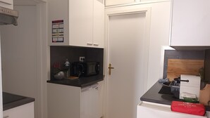 Une cuisine de taille réduite, avec des meubles blancs, un four à micro-ondes, un grille-pain et un réfrigérateur.