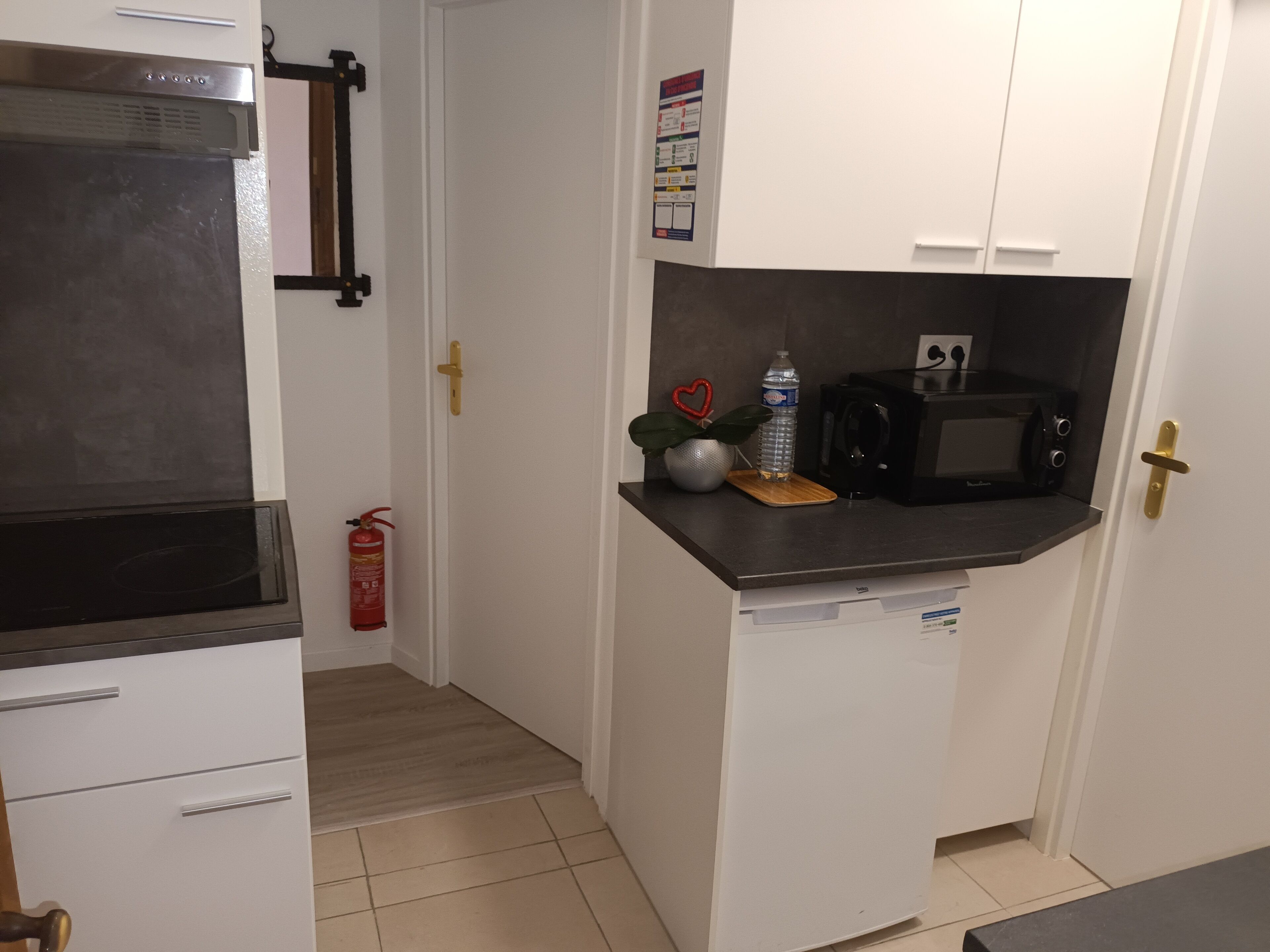 A compact kitchen with a microwave, a water bottle, and a fire extinguisher.