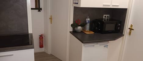 A compact kitchen with a microwave, a water bottle, and a fire extinguisher.
