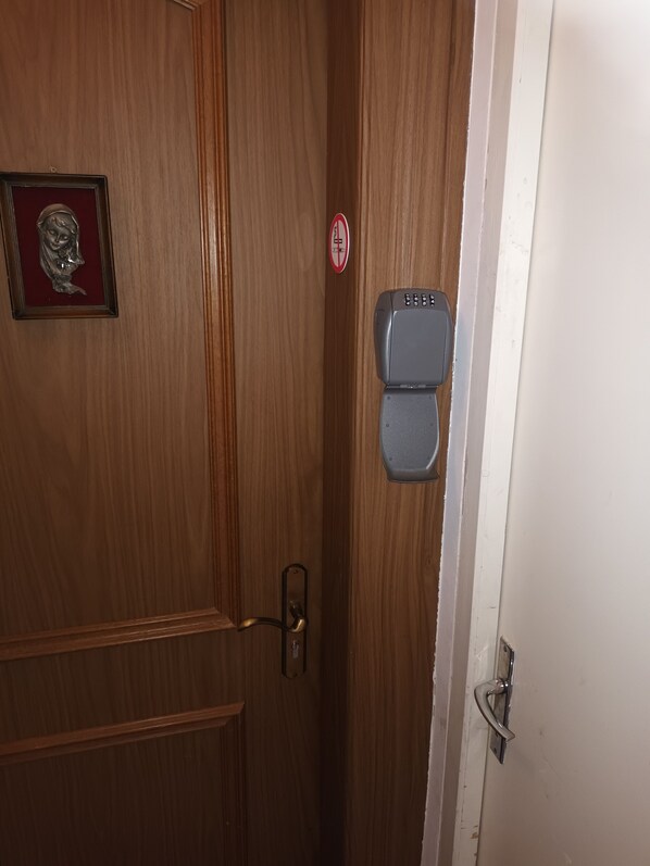 A wooden door with a brass handle, a no-smoking sign, and a keypad lock.