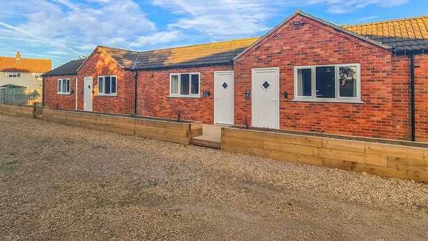 A row of brick buildings with white doors and windows, a gravel driveway, and a clear blue sky. - 1 bedroom accommodation in Walcott (Walcott)