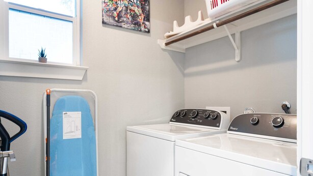 A laundry room with a washing machine, a dryer, and a blue ironing board. - Upstay Entertainment Hub Games & Firepit (Austin)