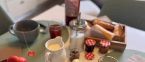 En frukostuppläggning med en tallrik pannkakor, en skål med frukt, en flaska juice, en kopp kaffe och en liten burk med sylt.