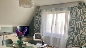 A modern living room with a dining area, a television, and a large window with patterned curtains. - Downtown, Enclosed private parking lot, Bike storage area (Mayenne)