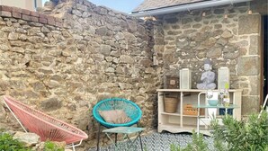 A stone wall, a wicker chair, a small table with a cushion, and a statue. - Downtown, Enclosed private parking lot, Bike storage area (Mayenne)