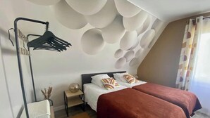 A bedroom with two beds, a hanging light fixture, and a wall with circular patterns. - Downtown, Enclosed private parking lot, Bike storage area (Mayenne)