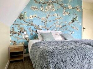 A bedroom with a bed, pillows, a nightstand, and a wall with a floral mural. - Downtown, enclosed private parking lot, bicycle storage room (Mayenne)