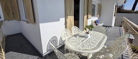 En udendørs terrasse med et hvidt bord og stole, en lille plantekasse og en dekorativ væg.