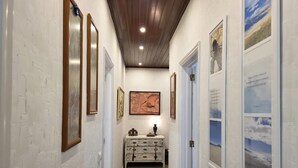A hallway with white brick walls, wooden ceiling, and framed artwork.