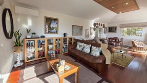 A spacious living room with a brown leather sofa, wooden coffee table, and a bookshelf filled with books and decorative items.