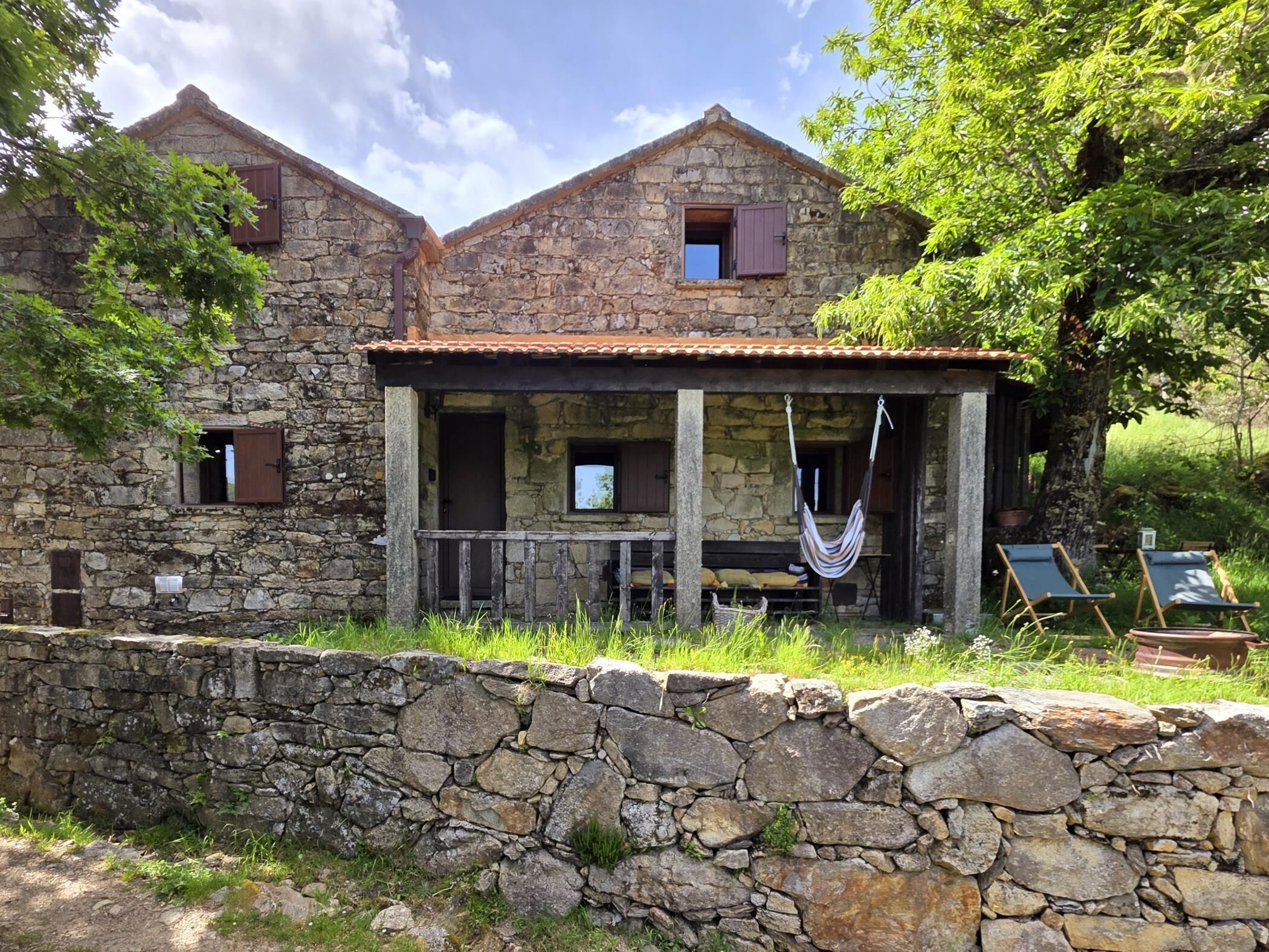 Un bâtiment en pierre doté d’un porche, d’un hamac et de deux fauteuils de jardin.
