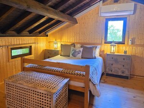Une chambre à coucher dans un chalet en bois, comprenant un lit, des tables de chevet, une commode, un banc et un téléviseur.