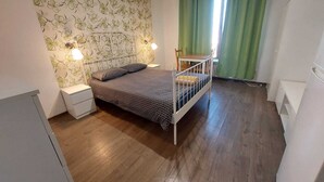 A small, well-lit bedroom with a single bed, a nightstand, a dresser, and a window with green curtains. - Vasile Apartment studio  (Bucharest)