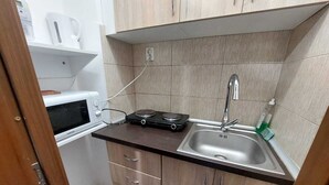 A compact kitchen with a microwave, a stove, a sink, and wooden cabinets. - Vasile Apartment studio  (Bucharest)