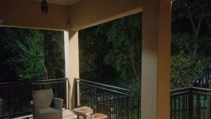 Ein Balkon mit Korbmöbeln, einem Glastisch und Blick auf Bäume.
