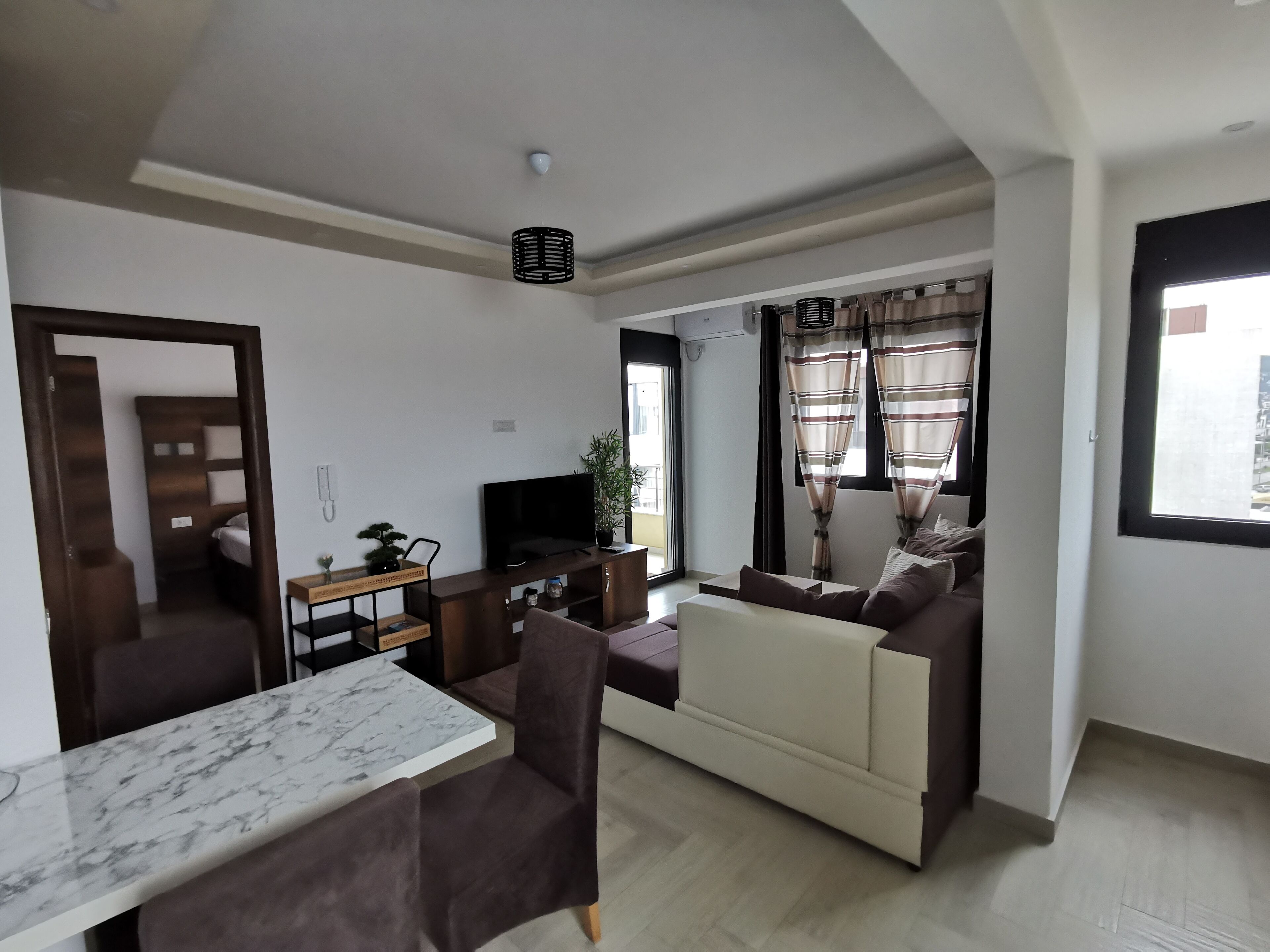 Een moderne woonkamer met een bank, een televisie, een marmeren tafel en een kleine plant.