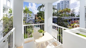 Un balcon avec une table et des chaises blanches, une plante en pot et une vue sur des palmiers et des immeubles.