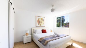 Une chambre à coucher avec un lit, une table de chevet, une lampe et une fenêtre donnant sur un paysage verdoyant.